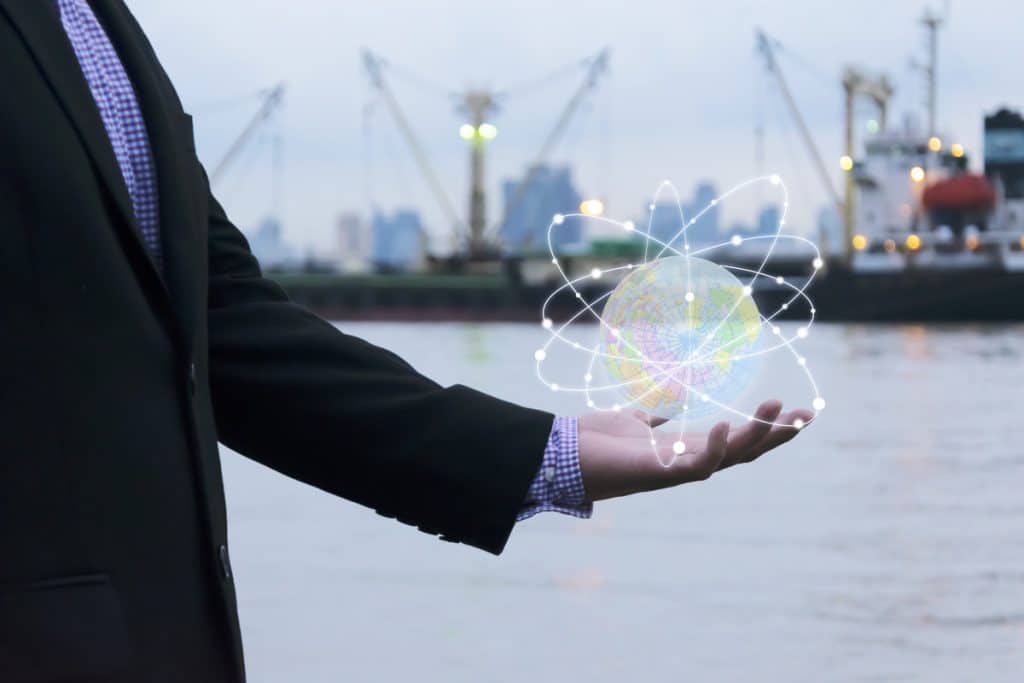 A Businessman wearing a black suit is working with a glowing globe in his hand, surrounded by orbits, representing worldwide shipping and distribution growth.